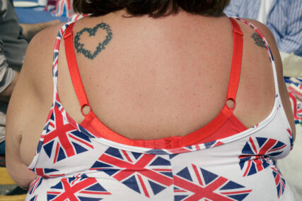 Close-up view of a woman's back showing her union flag dress, her bare upper back, bra straps and love heart tattoo.