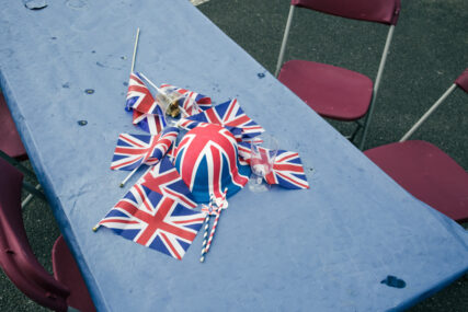 Union jack flags and a hat are left on a blue paper table covering on a trestle table after a coronation picnic.