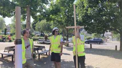 L-R: Alex Zoboli, Angelo Leonardo and Hugo Weber wearing high-vis vests and discussing how to install the prints. Hugo is carrying a large wooden cross which was part of our installation method.