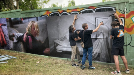 Alex, Hugo and Angelo hold a poster in place and staple it to the wooden hoardings.