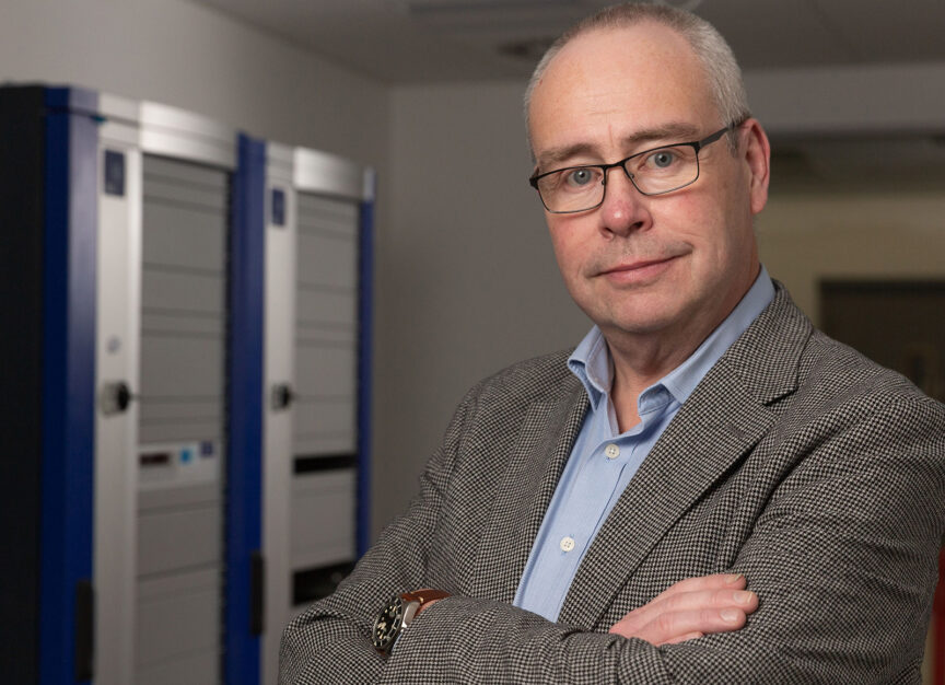 Relaxed portrait of Professor Rob Oliver of IAAPS with computer cabinets visible behind him.