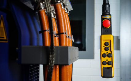 Photo of orange and blue hydraulic lines connected to machinery terminals on the left of the photo with a yellow winch hand controller on the right.