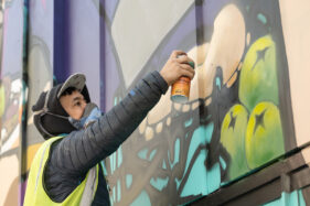 Graffiti artist Silent Hobo is wearing a baseball cap and respirator mask as he spray paints a mural onto a wall in Bristol.