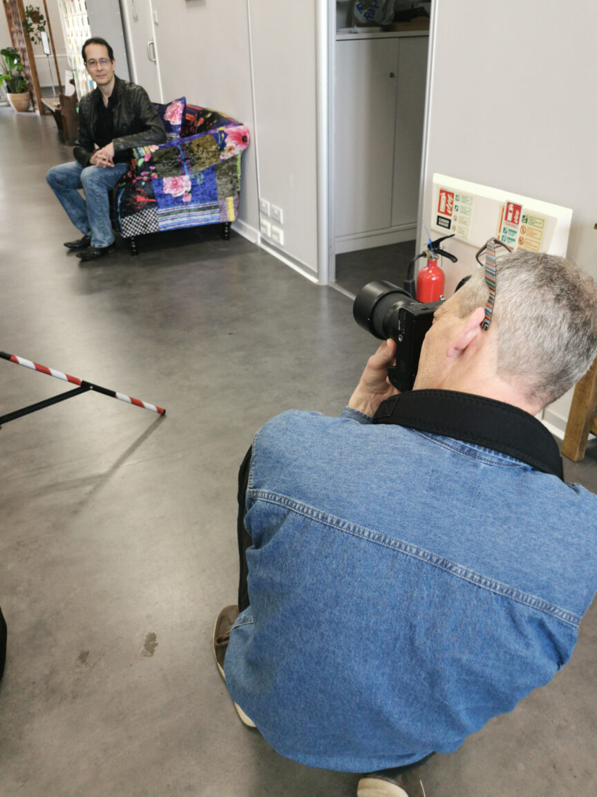 I'm crouching in a corridor photographing Paul Albone who's sitting on a colourful sofa.