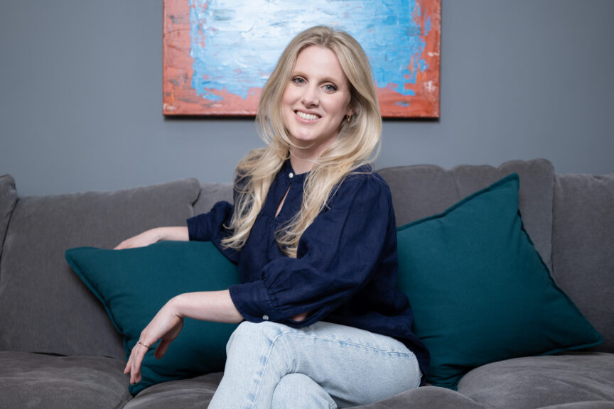 Stefanie Blundell is seated casually on a comfy sofa, smiling to camera.