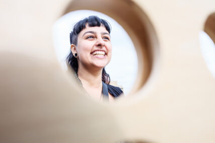 A young female student is smiling into the distance and she is pictured through a hole in a Connect 4 game board.