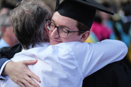 A University of Bath graduate hugs his dad. He has a look of relief on his face.