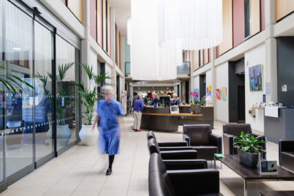 The Sulis Hospital Bath reception area with comfy seating, reception desk and hanging net curtains designed to bring light into the space. I blurred nurse is walking through the scene.