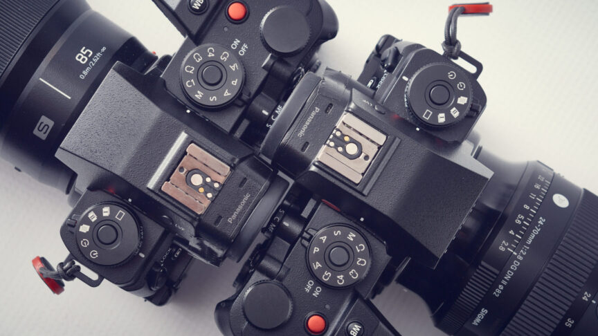 A top-down view of two Panasonic Lumix camera bodies placed back-to-back showing that the controls and design are identical, even though they are two different models of camera.